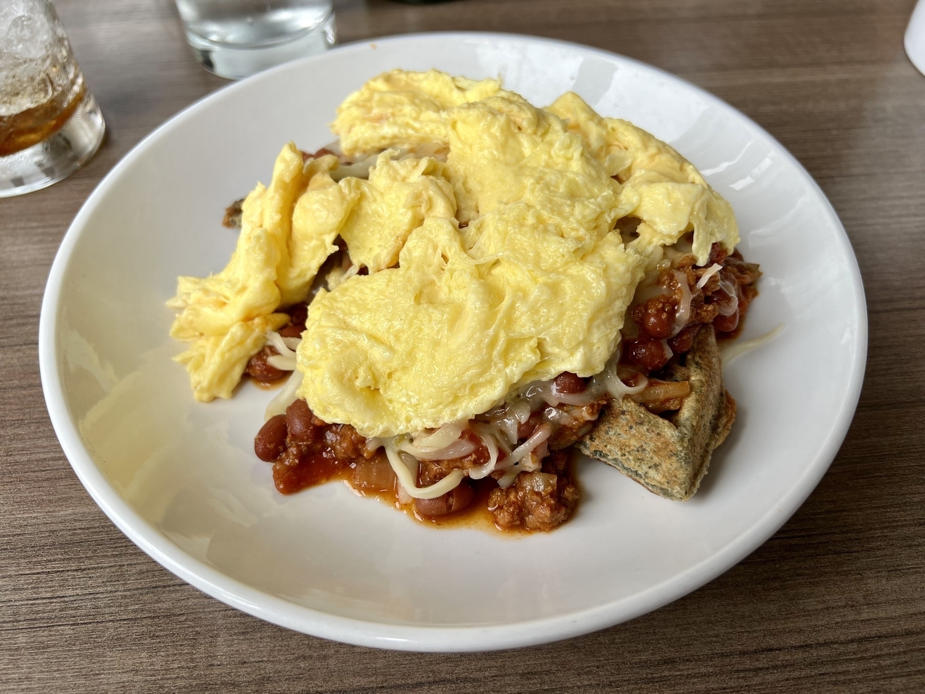 Veggie Slinger: corn-flour waffle, impossible “meat” chili, Swiss cheese, and scrambled eggs…on a plate.