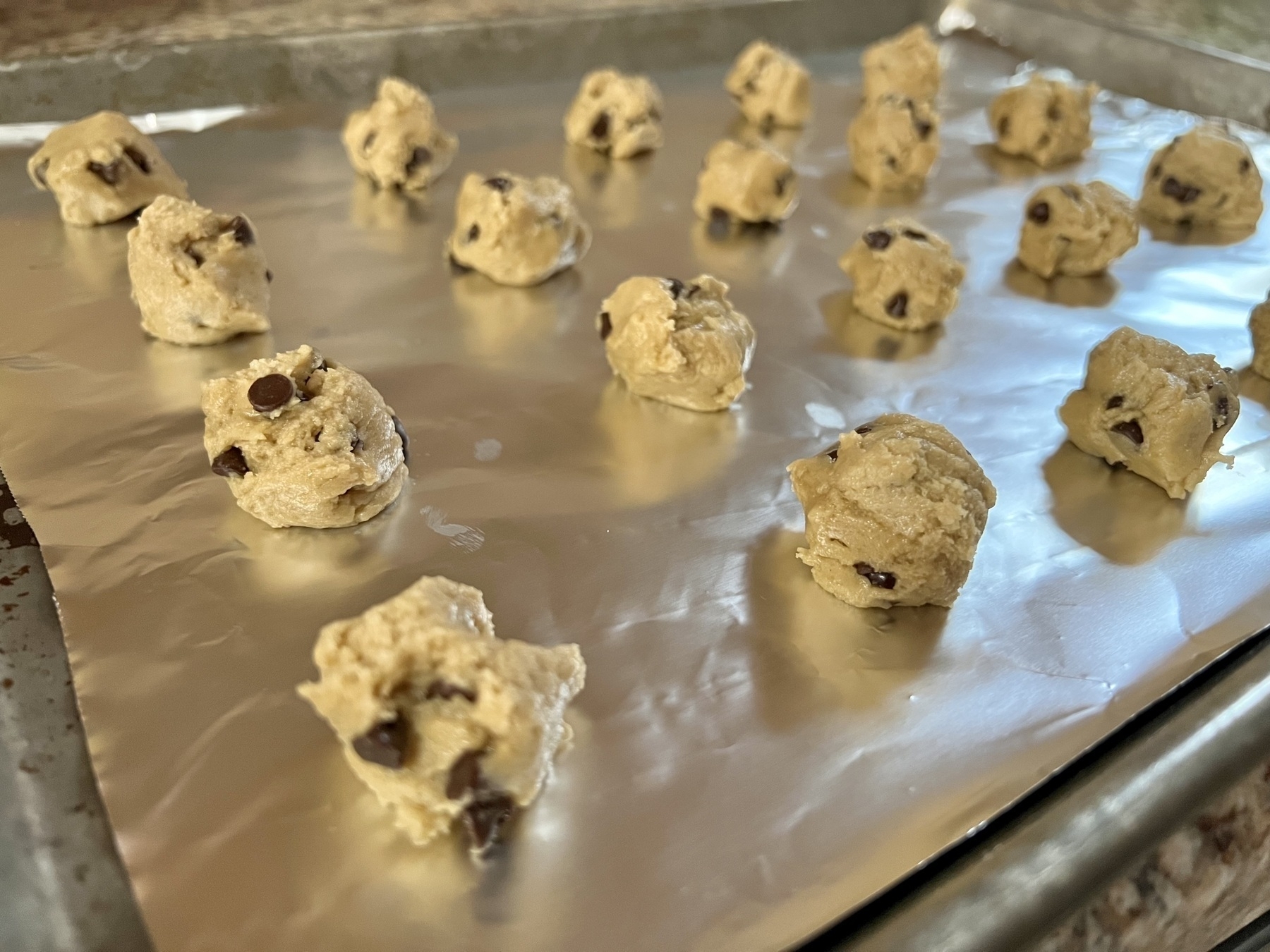 Rows of raw cookie dough on a baking sheet, before going into the oven.