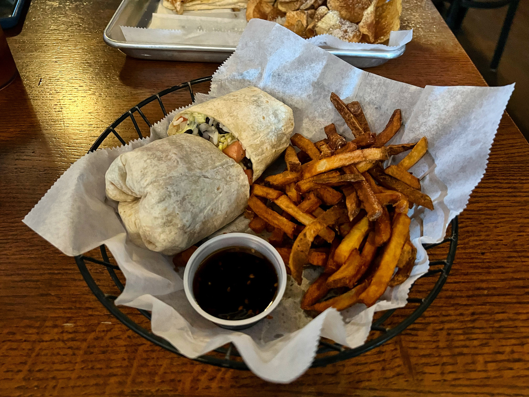 Veggie wrap (with fish) and fries with teriyaki sauce, in a wire basket on top of serving paper.