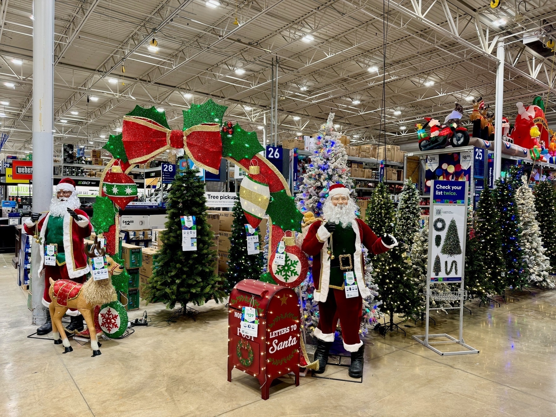 Christmas display at a hardware store: two Santa's standing in front of a series of pre-lit Christmas trees (some green, some sprayed with fake snow), and a giant arch made of holly, ribbons and bows.
