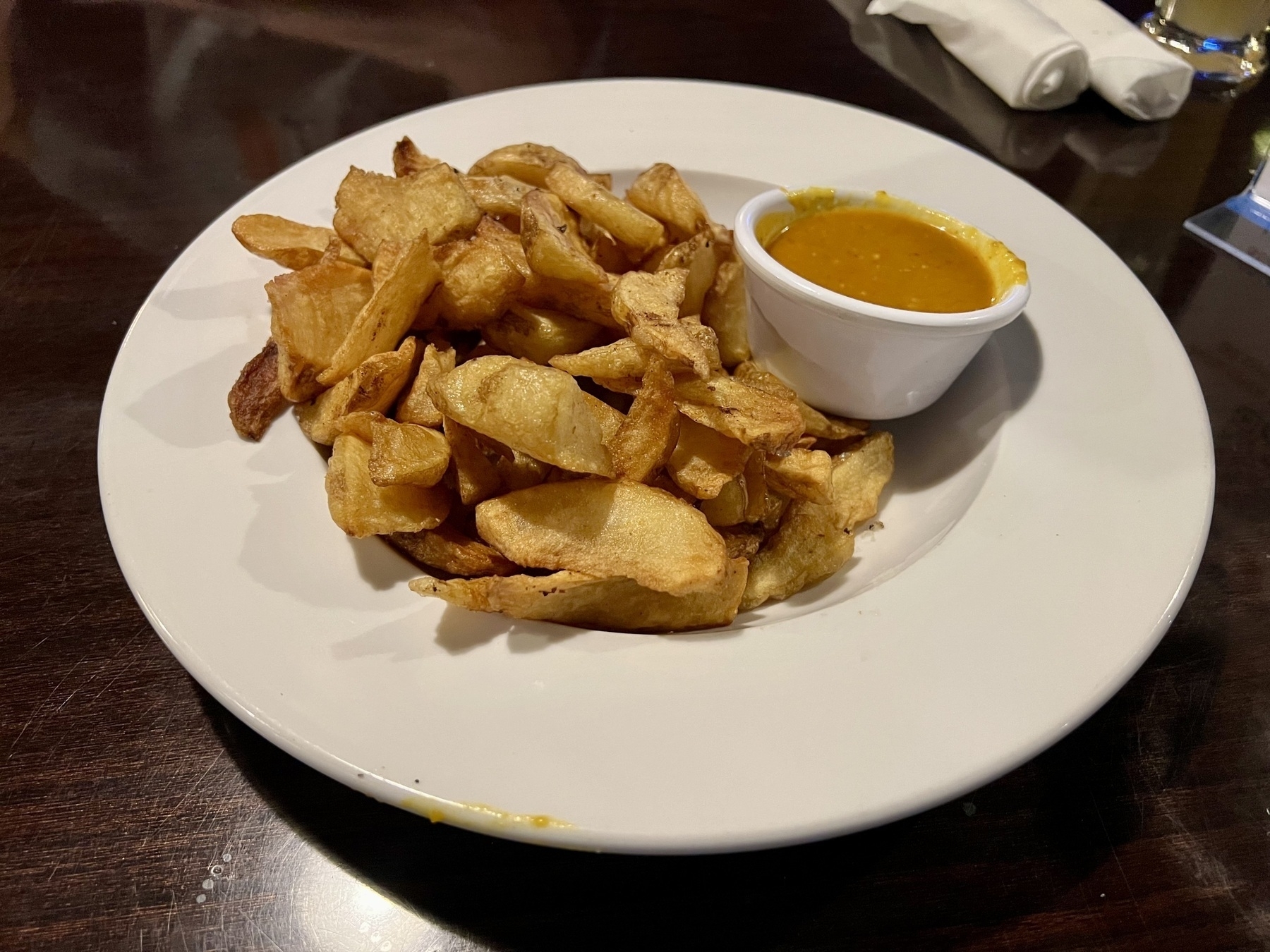 Wedge-shaped fries on a circular white plate, with a yellow-orange curry sauce on the site, in a small ramekin.