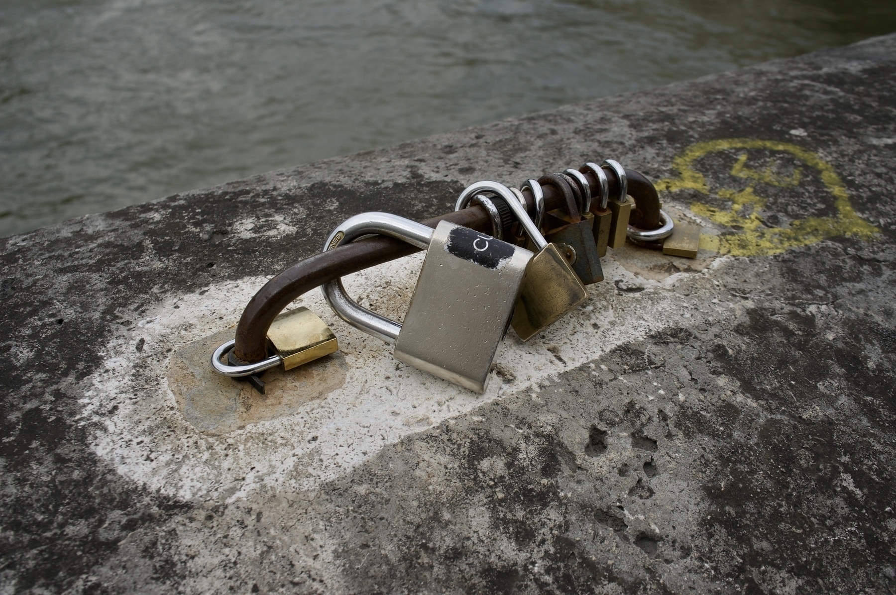 Series of locks on a rail, on a bridge, with a slight view of the river below, in Paris.