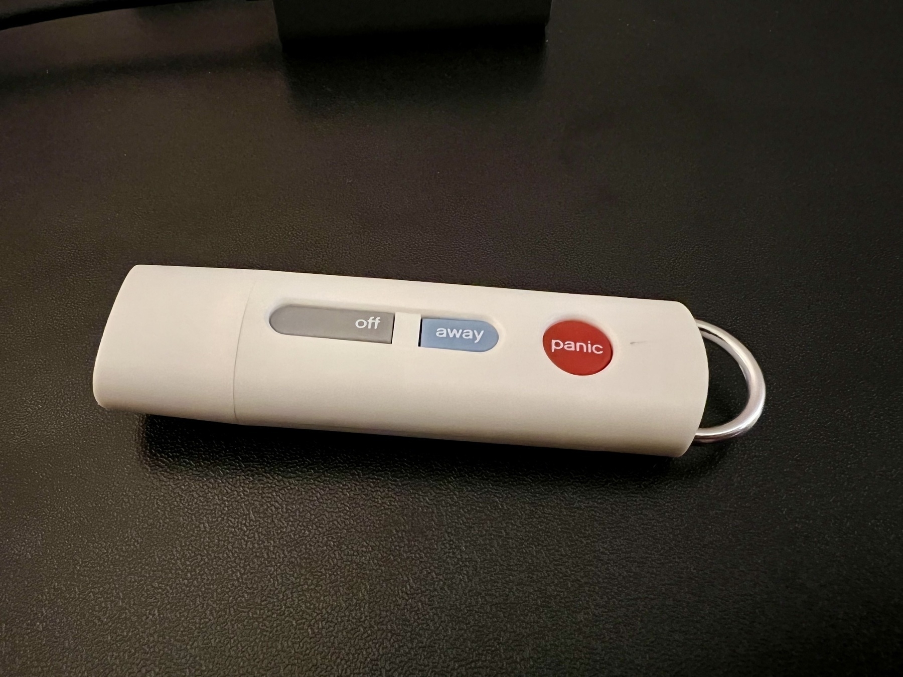 Plastic dongle on a table, with three buttons on it; 'off' in grey, 'away' in blue, and 'panic' in red.
