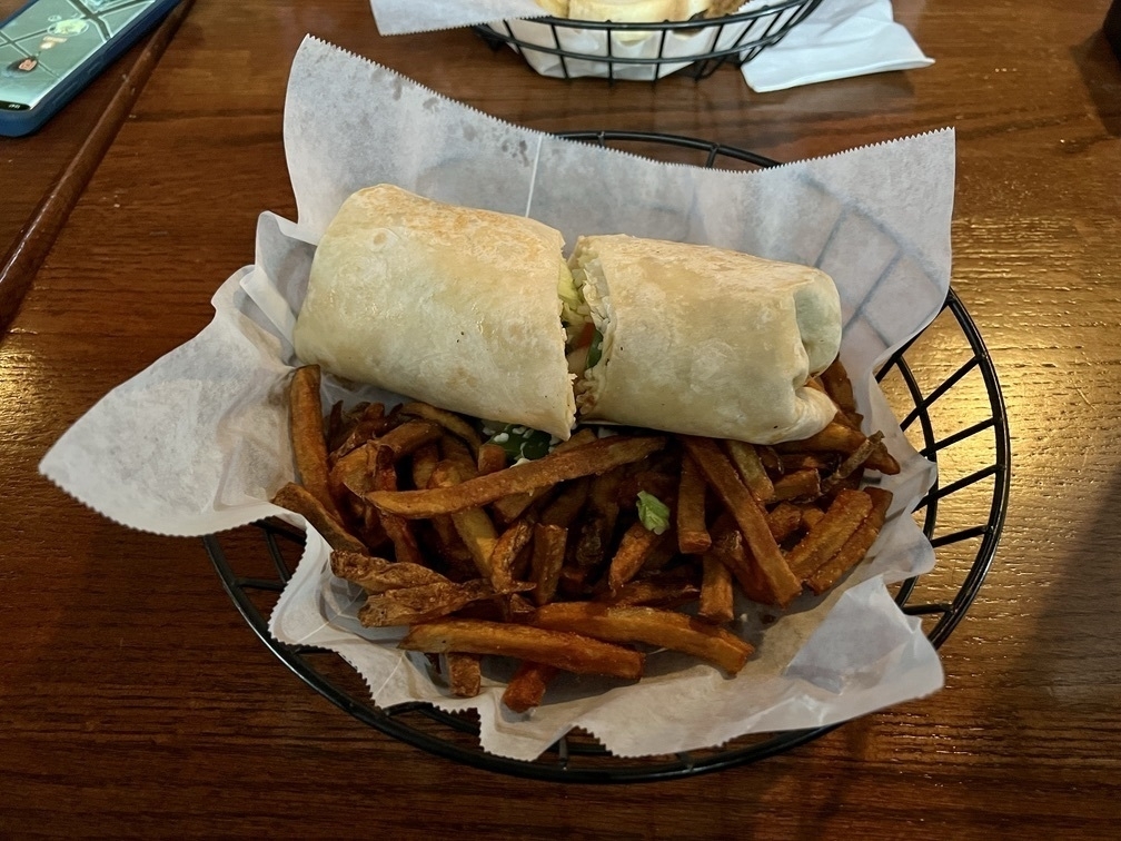 Photo of a veggie wrap with fries, in a basket on a table.