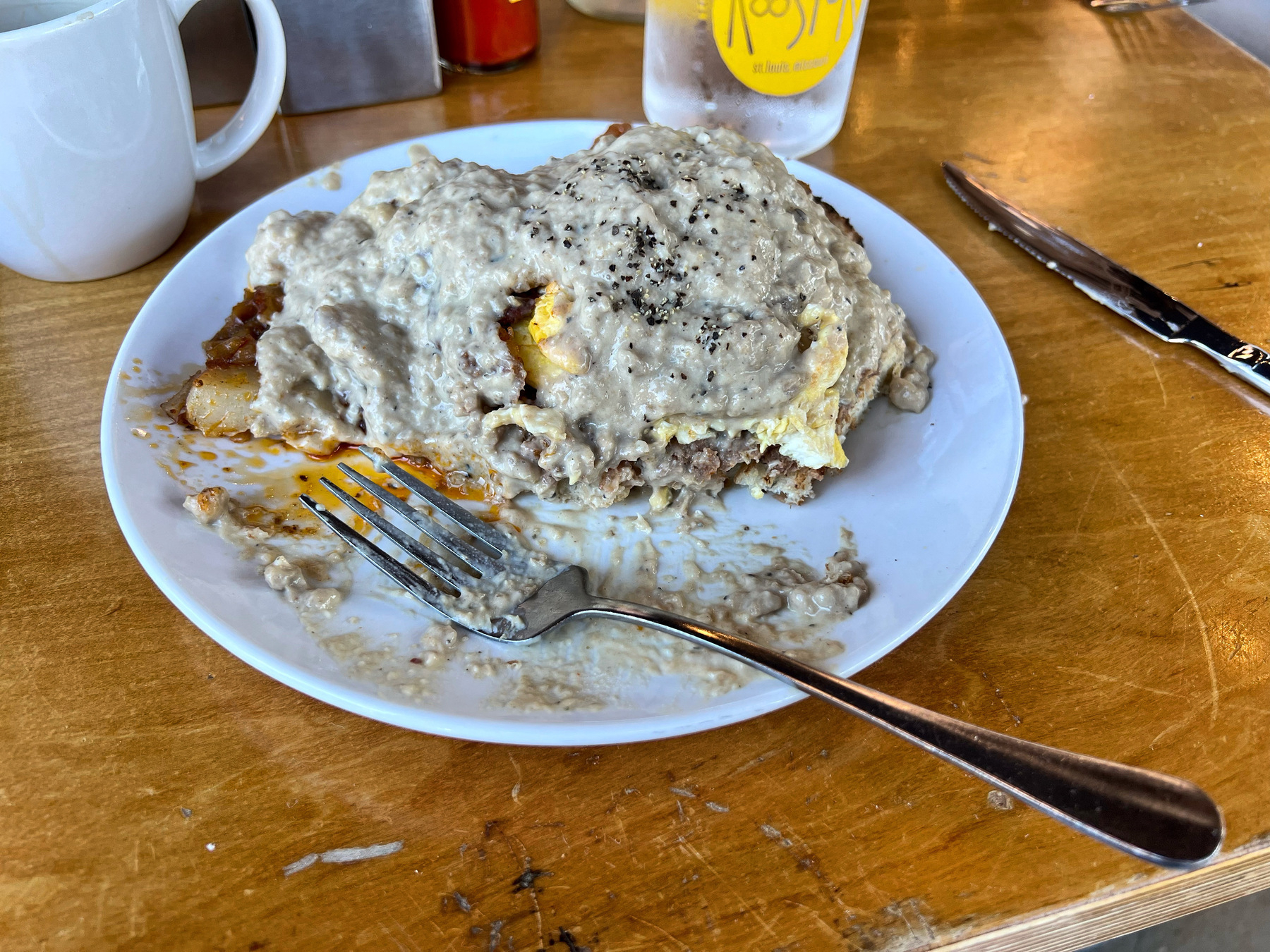 Vegan slinger (sourdough toast, vegetarian sausage, and scrambled eggs, covered in gravy) on a white plate with a fork.